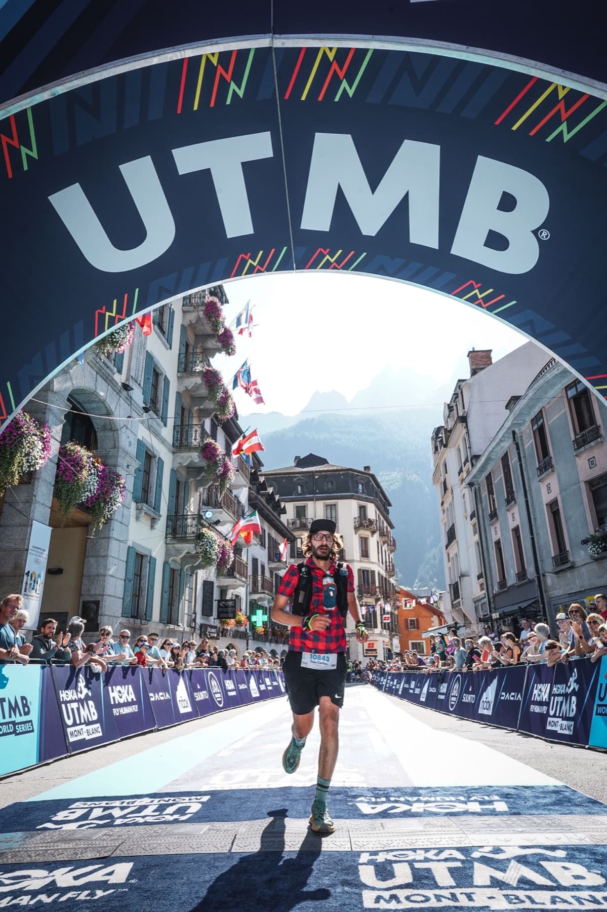 Luis runs to the TDS finish in Chamonix, under the UTMB arch, with mountains behind.