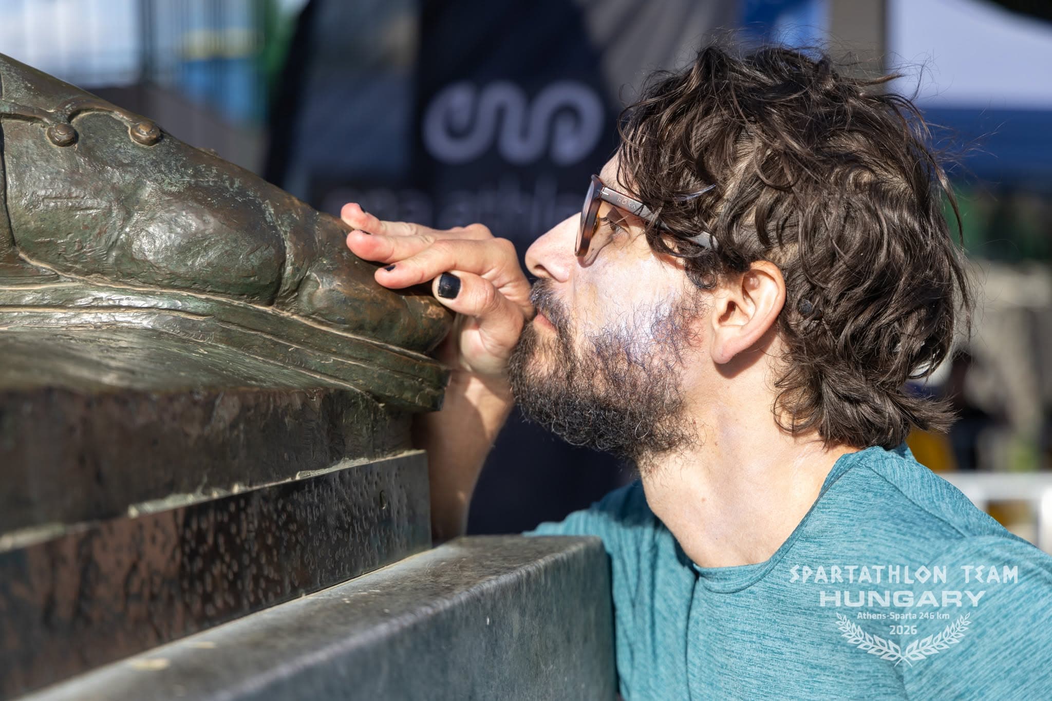 The author, seen from the side, kisses the bronze foot of the statue of Leonidas.