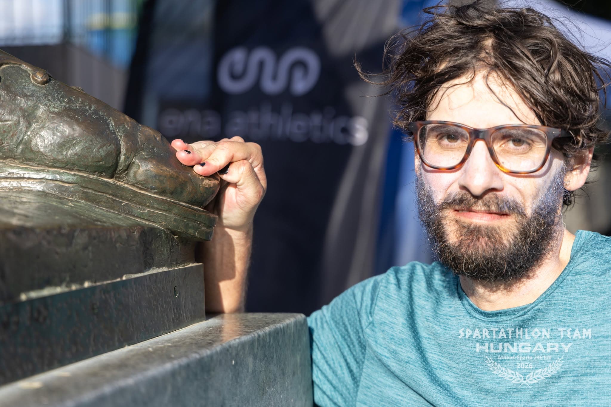The author looks at the camera, tired and calm, with his hand on the bronze foot of Leonidas.